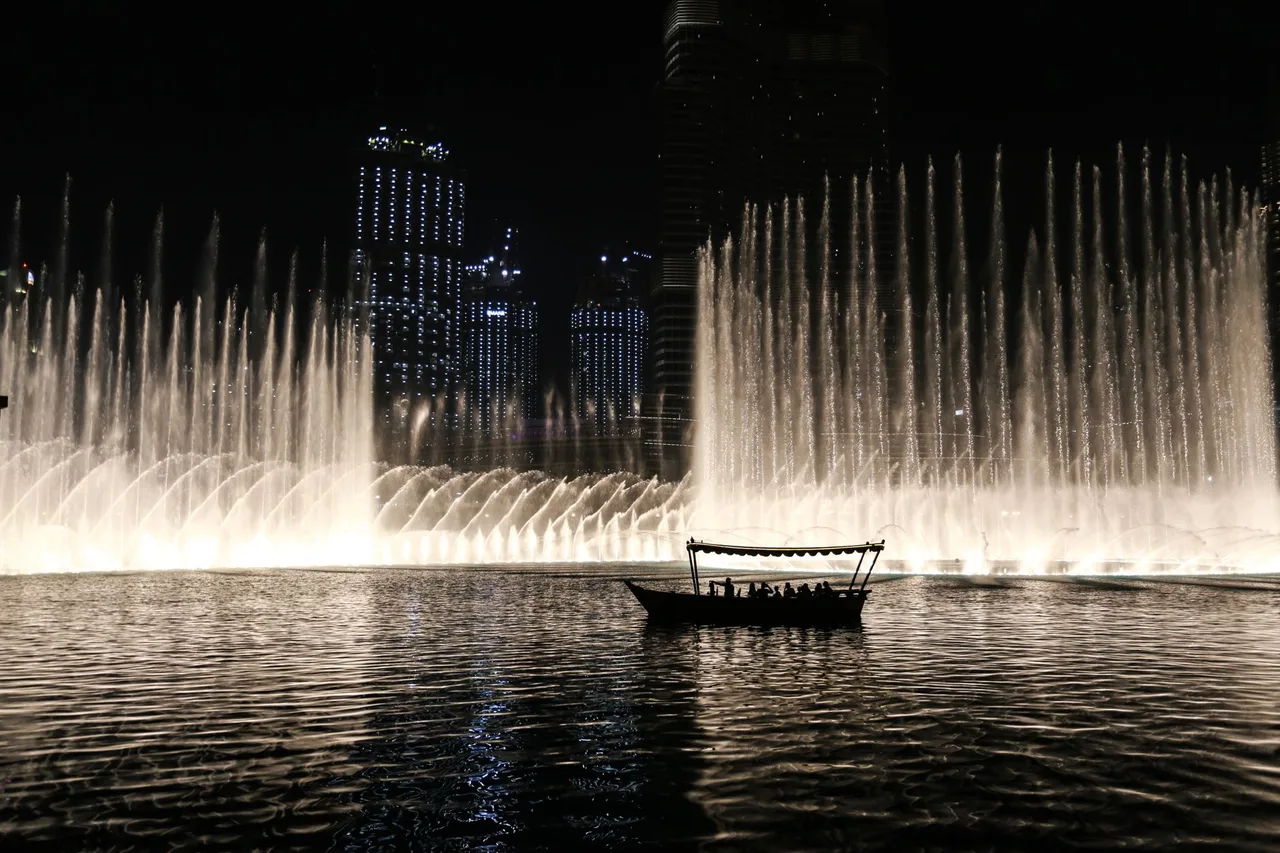 Dubai Fountain: Kompletní průvodce tančící fontánou u Burj Khalifa Silueta tradiční loďky abra před tryskami Dubai Fountain v noci