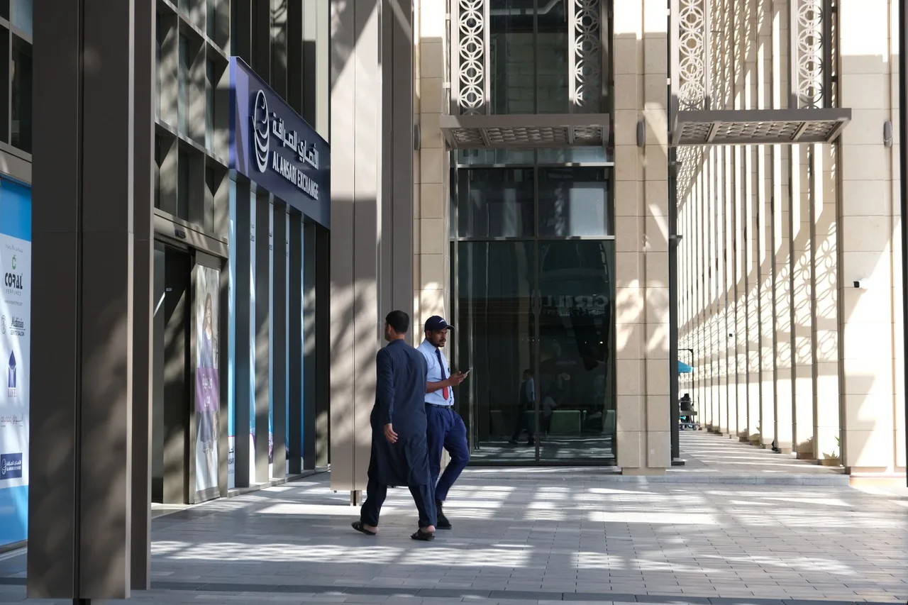 Muži v tradičním emirátském oděvu procházejí kolem moderní administrativní budovy v obchodní čtvrti Dubaje.