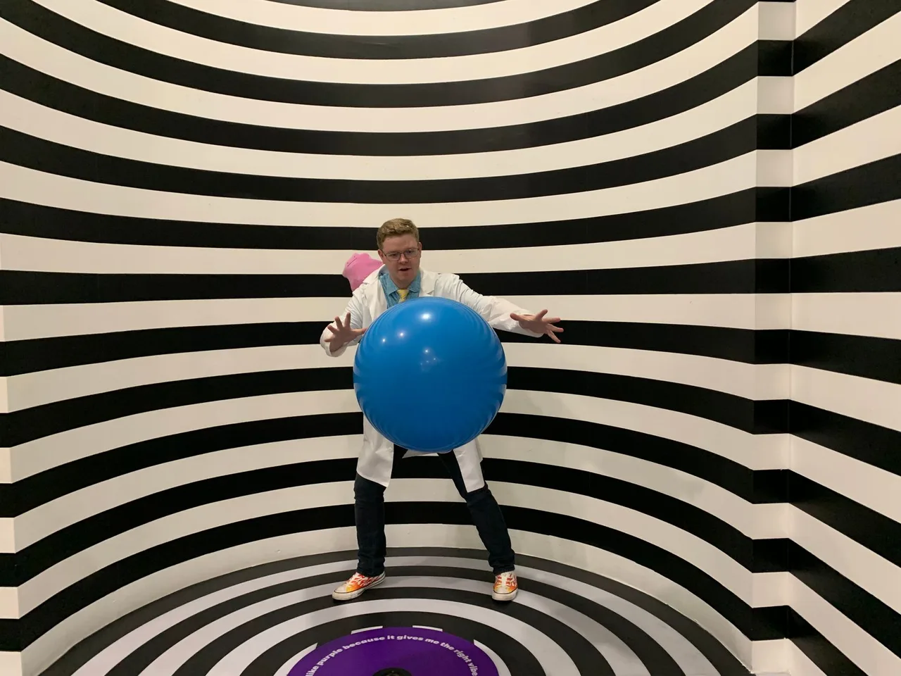 Museum of Illusions Dubai: Iluze a Optické Klamy v Al Seef Návštěvník v pruhované iluzivní místnosti drží modrý míč, typický exponát optického klamu