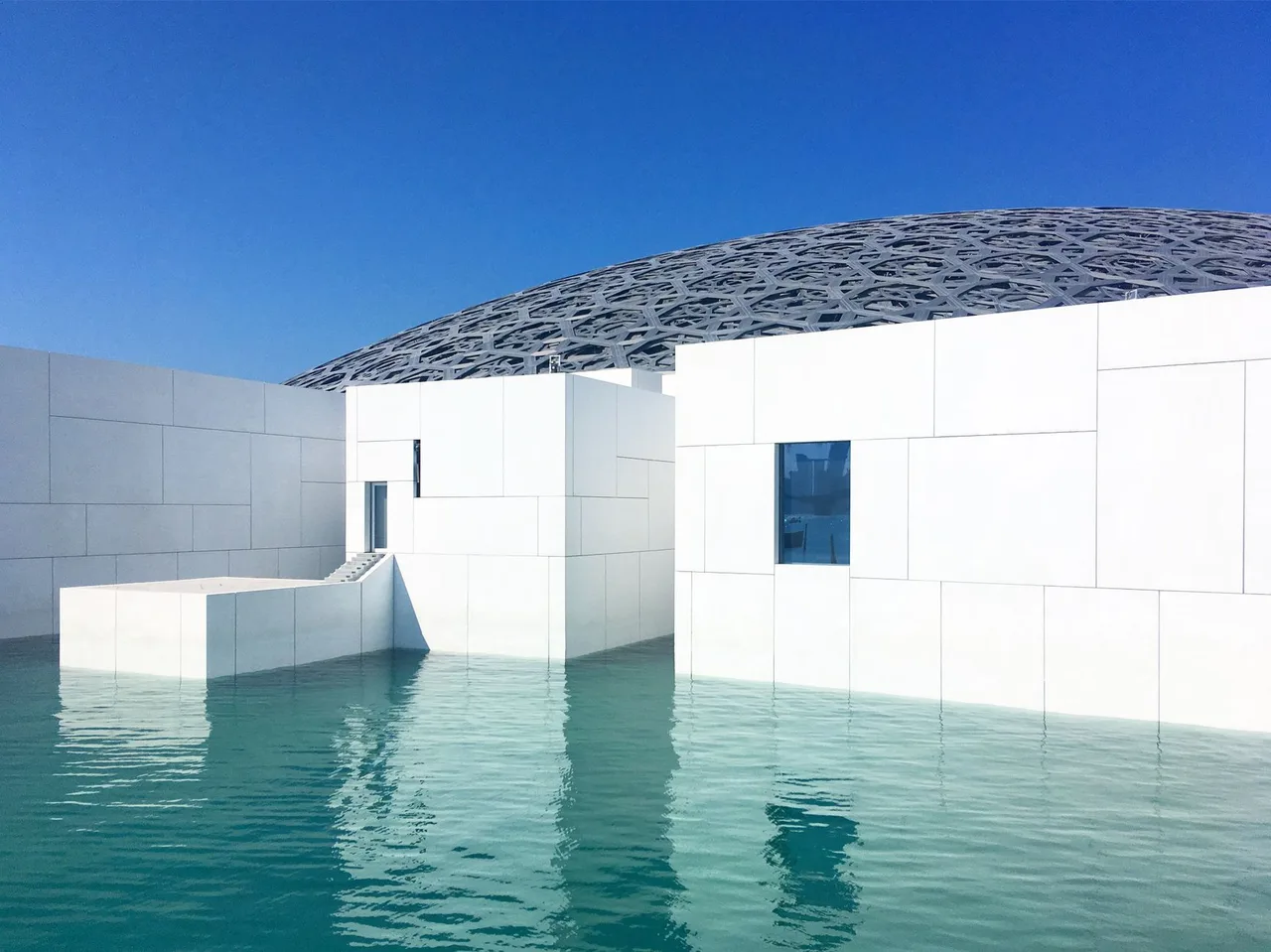 Bílé budovy Louvre Abu Dhabi obklopené vodou v Saadiyat Cultural District