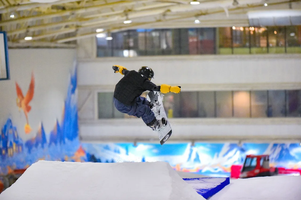Snowboardista ve výskoku nad překážkou v kryté sněhové hale