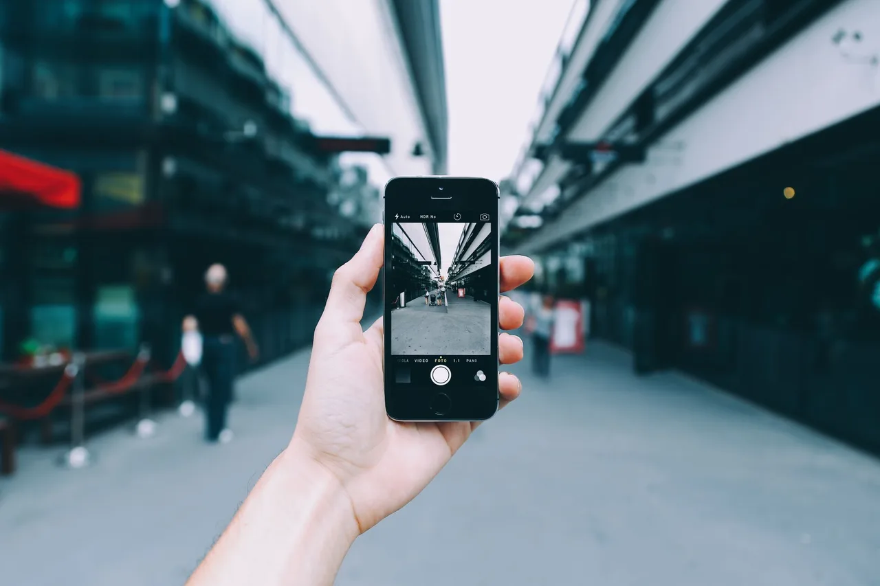 Ruka drží telefon a fotografuje kolemjdoucí lidi na ulici
