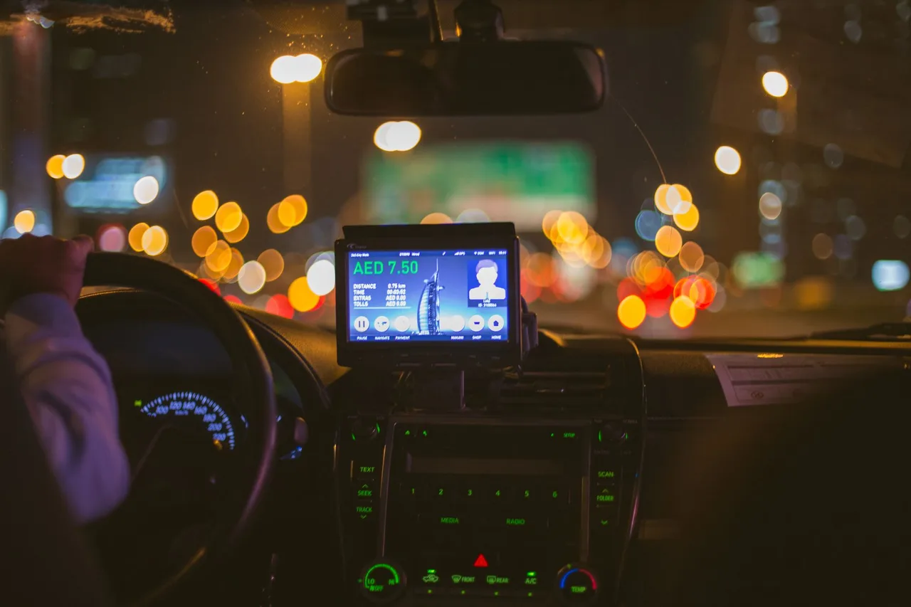 Taxi v Dubaji: Careem, Uber a ceny jízd Displej na palubní desce vozu v noci ukazuje cenu jízdy v aplikaci, v pozadí rozostřená světla Dubaje